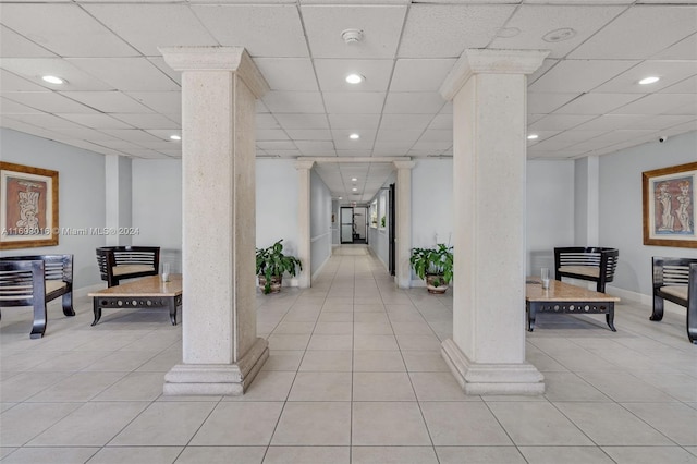 hall with a paneled ceiling, ornate columns, and light tile patterned flooring