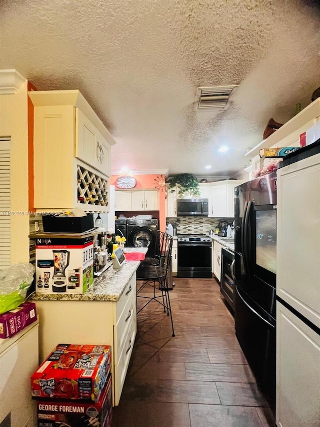 kitchen with black fridge, washer and clothes dryer, white cabinets, dark hardwood / wood-style floors, and range with electric stovetop