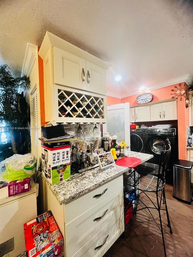 kitchen featuring washing machine and dryer, white cabinetry, crown molding, and light stone countertops