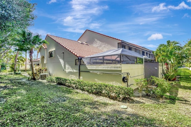 view of home's exterior with central AC unit, glass enclosure, and a yard