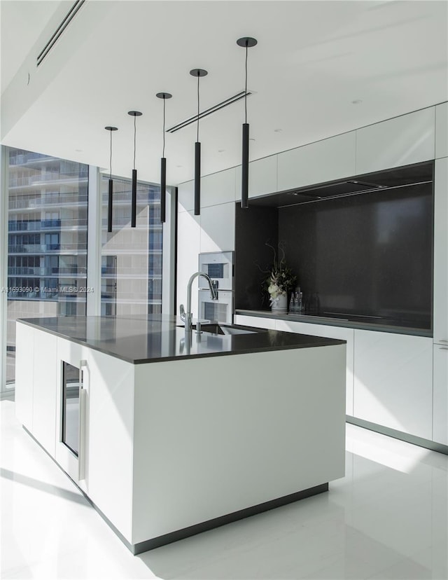 kitchen with pendant lighting, white cabinetry, a kitchen island with sink, and beverage cooler