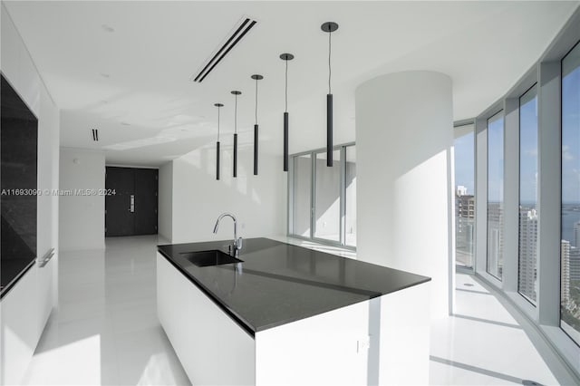 kitchen featuring sink, hanging light fixtures, expansive windows, a kitchen island with sink, and white cabinets