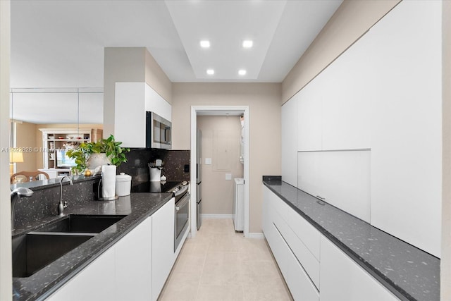 kitchen featuring backsplash, sink, dark stone countertops, white cabinetry, and stainless steel appliances