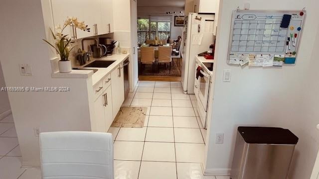 kitchen featuring white cabinetry, sink, light tile patterned floors, and white appliances