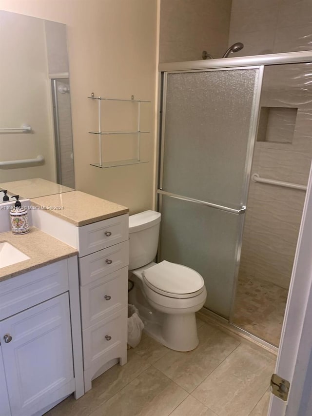 bathroom featuring tile patterned floors, vanity, toilet, and a shower with shower door