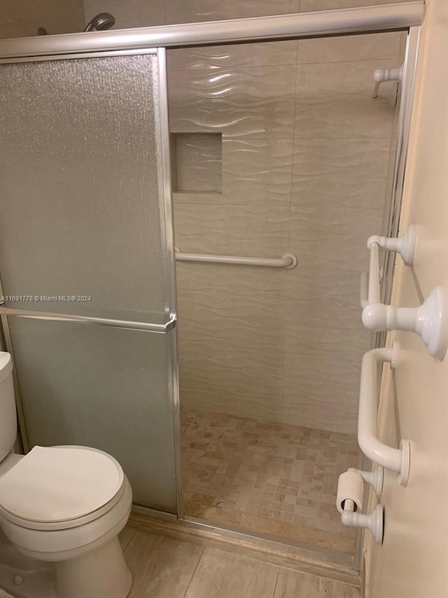 bathroom featuring tile patterned floors, a shower with door, and toilet