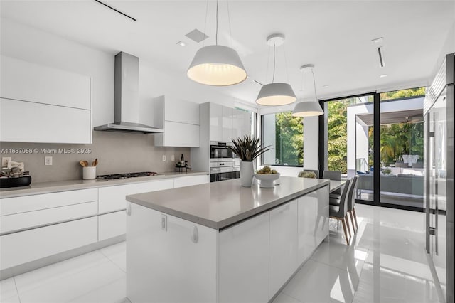 kitchen with decorative light fixtures, white cabinetry, a center island, stainless steel appliances, and wall chimney range hood