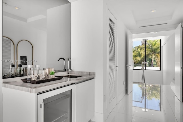 bar with white cabinetry, sink, beverage cooler, and a raised ceiling