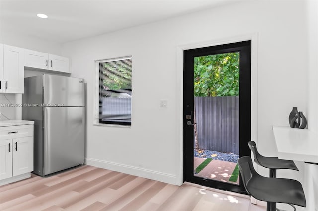 kitchen featuring stainless steel fridge, light wood-type flooring, white cabinetry, and light stone counters