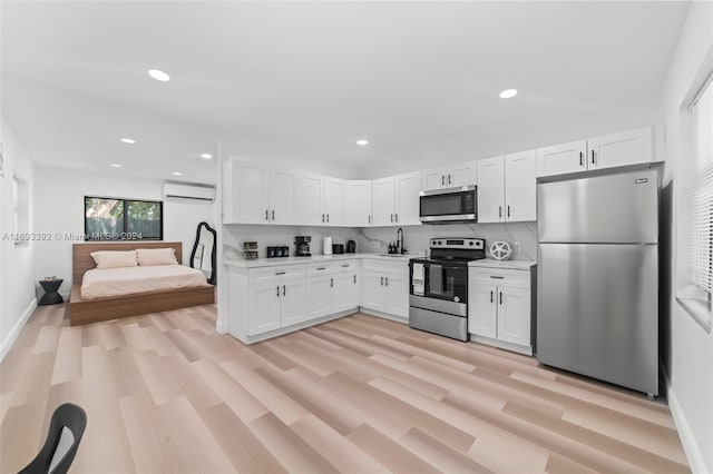 kitchen with decorative backsplash, appliances with stainless steel finishes, a wall mounted AC, light hardwood / wood-style floors, and white cabinetry