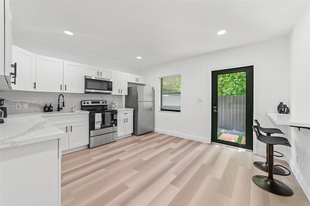 kitchen with white cabinets, sink, appliances with stainless steel finishes, light hardwood / wood-style floors, and light stone counters