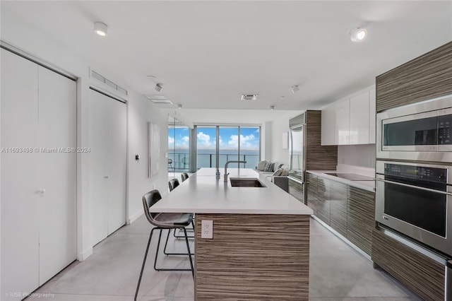 kitchen with a kitchen island with sink, white cabinets, a kitchen breakfast bar, sink, and stainless steel appliances