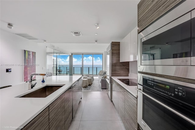 kitchen featuring white cabinets, a water view, sink, light tile patterned floors, and appliances with stainless steel finishes