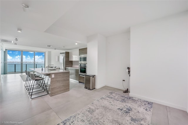 kitchen with sink, a kitchen island, a water view, a breakfast bar, and white cabinets