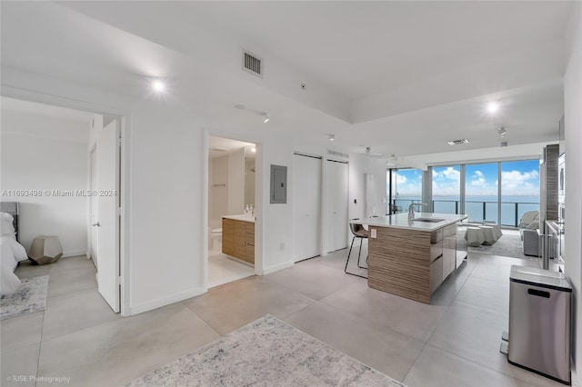 kitchen with a breakfast bar, electric panel, a center island with sink, a water view, and sink