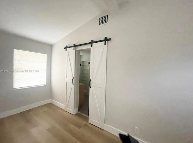 interior space with a barn door, vaulted ceiling, and light wood-type flooring