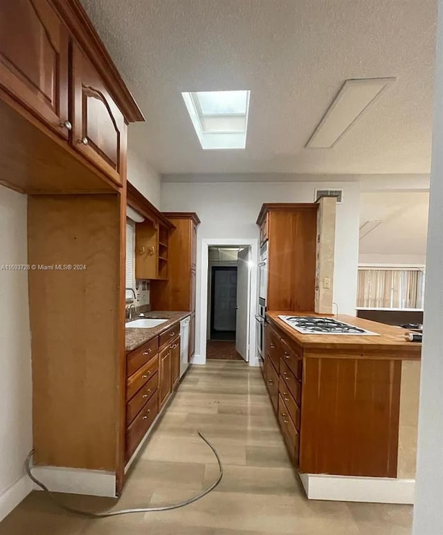 kitchen with stainless steel dishwasher, a textured ceiling, white gas cooktop, sink, and light hardwood / wood-style floors