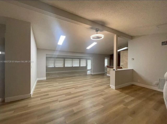 additional living space with lofted ceiling with beams, a textured ceiling, and light hardwood / wood-style flooring