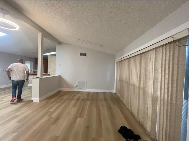 interior space featuring a textured ceiling, light hardwood / wood-style flooring, and lofted ceiling