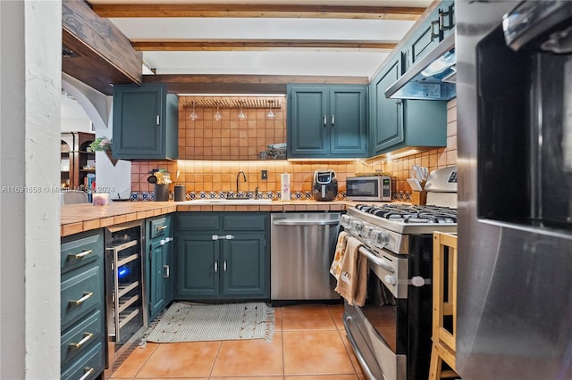 kitchen with beverage cooler, beam ceiling, appliances with stainless steel finishes, light tile patterned floors, and tile counters