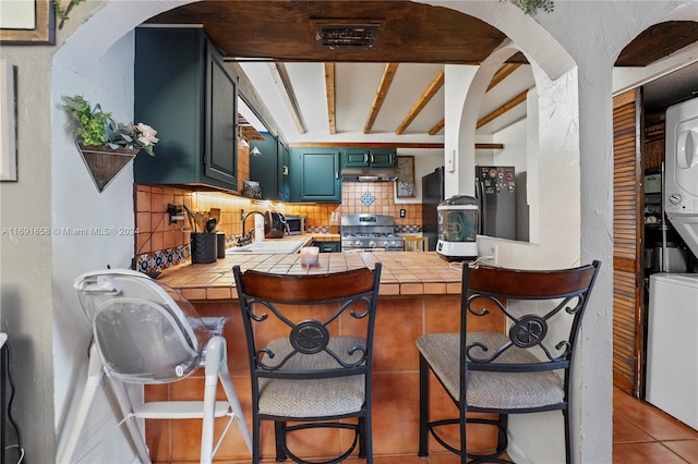 kitchen with a kitchen breakfast bar, tasteful backsplash, sink, stainless steel range oven, and tile counters