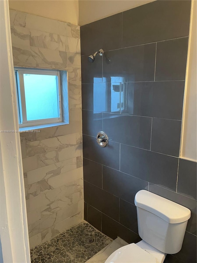 bathroom featuring toilet, tiled shower, and tile walls