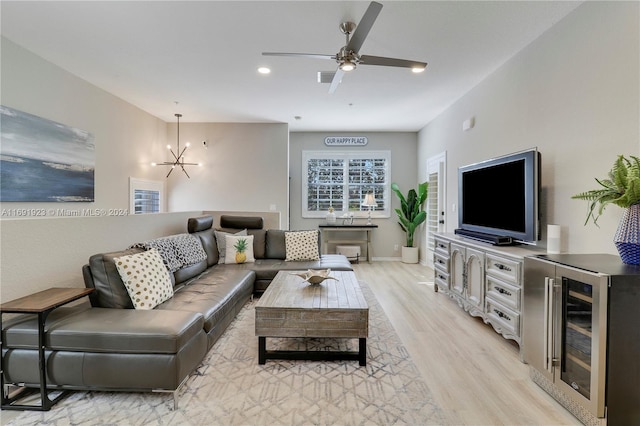 living room with wine cooler, ceiling fan with notable chandelier, and light hardwood / wood-style flooring