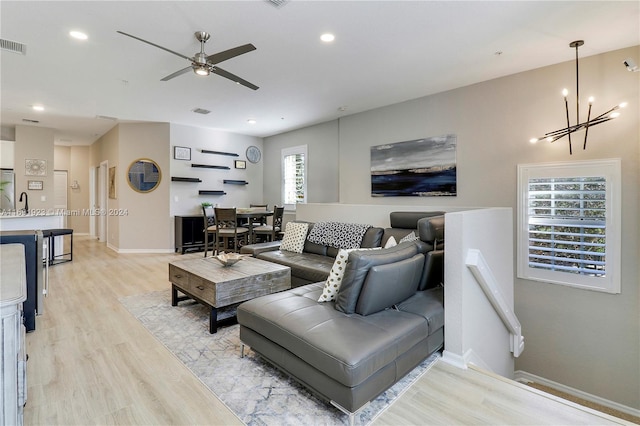 living room featuring ceiling fan with notable chandelier and light hardwood / wood-style flooring