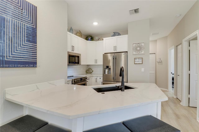 kitchen with kitchen peninsula, decorative backsplash, light stone countertops, stainless steel appliances, and white cabinets