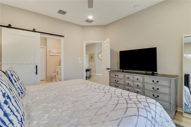 bedroom with a barn door, ensuite bathroom, ceiling fan, and light wood-type flooring