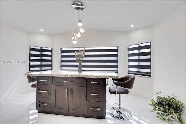 kitchen with light stone counters, dark brown cabinets, light tile patterned floors, decorative light fixtures, and a breakfast bar area