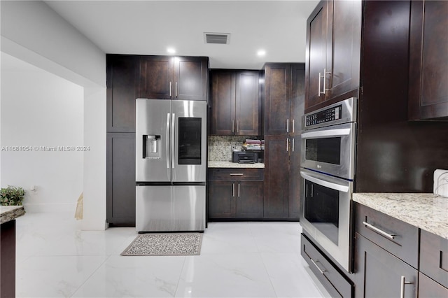 kitchen with backsplash, light stone countertops, dark brown cabinets, and appliances with stainless steel finishes