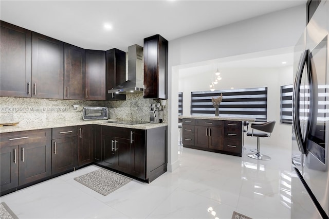 kitchen featuring dark brown cabinets, wall chimney range hood, backsplash, and stainless steel refrigerator