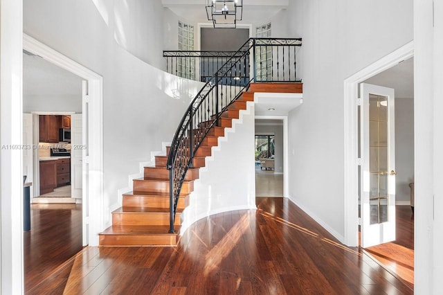 stairs with a notable chandelier, a towering ceiling, and wood-type flooring