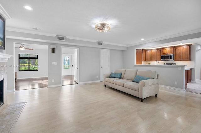 living room with light hardwood / wood-style flooring, crown molding, a fireplace, and ceiling fan