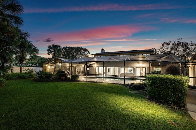 back house at dusk featuring a lanai and a lawn