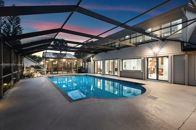 pool at dusk featuring a lanai and a patio area