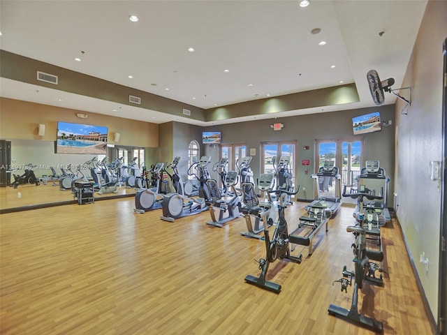 exercise room with a raised ceiling and light wood-type flooring