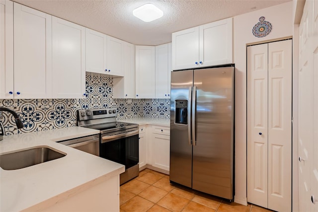 kitchen featuring white cabinetry, sink, decorative backsplash, light tile patterned floors, and appliances with stainless steel finishes