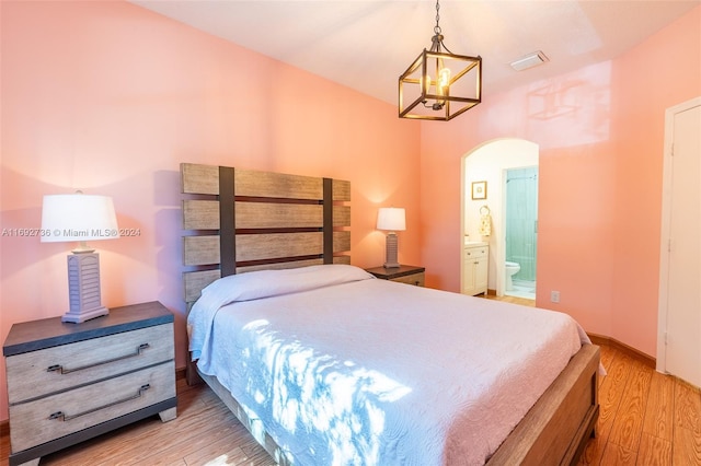 bedroom with light hardwood / wood-style flooring, connected bathroom, and a chandelier