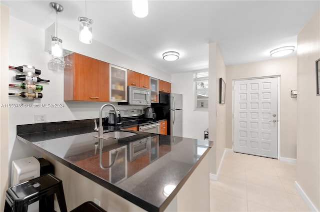 kitchen featuring kitchen peninsula, a breakfast bar, stainless steel appliances, decorative light fixtures, and dark stone countertops