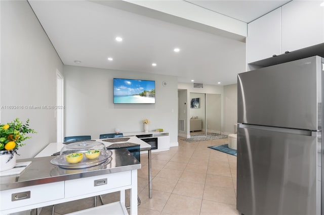 kitchen with stainless steel counters, light tile patterned floors, white cabinetry, and stainless steel refrigerator