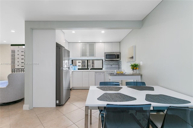 kitchen featuring decorative backsplash, white cabinetry, stainless steel appliances, and light tile patterned floors