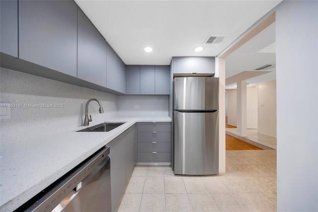 kitchen with gray cabinets, appliances with stainless steel finishes, sink, backsplash, and light stone counters