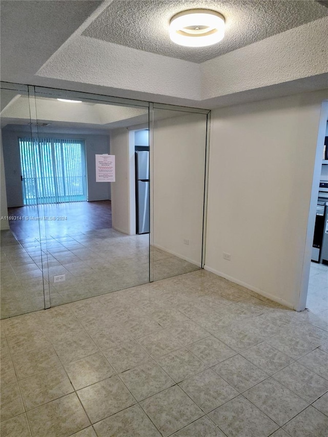 unfurnished room with light tile patterned floors, a textured ceiling, and a raised ceiling