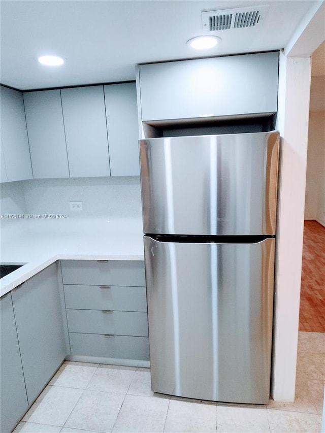 kitchen with stainless steel fridge, light tile patterned floors, and gray cabinetry