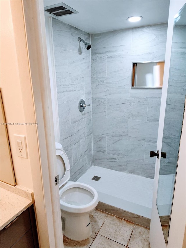 bathroom featuring a tile shower, tile patterned flooring, vanity, and toilet