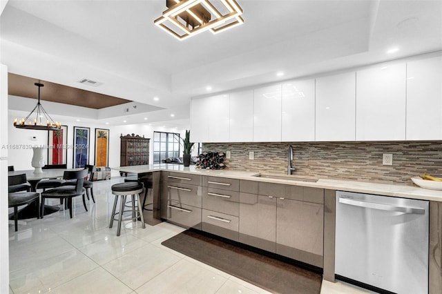 kitchen featuring stainless steel dishwasher, a raised ceiling, sink, pendant lighting, and white cabinets