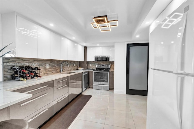 kitchen featuring sink, light tile patterned floors, appliances with stainless steel finishes, tasteful backsplash, and white cabinetry