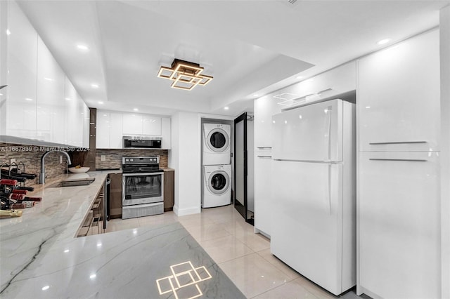 kitchen with light stone countertops, sink, stacked washing maching and dryer, stainless steel appliances, and white cabinets